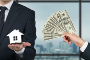 A man holding money and a house in front of a window.