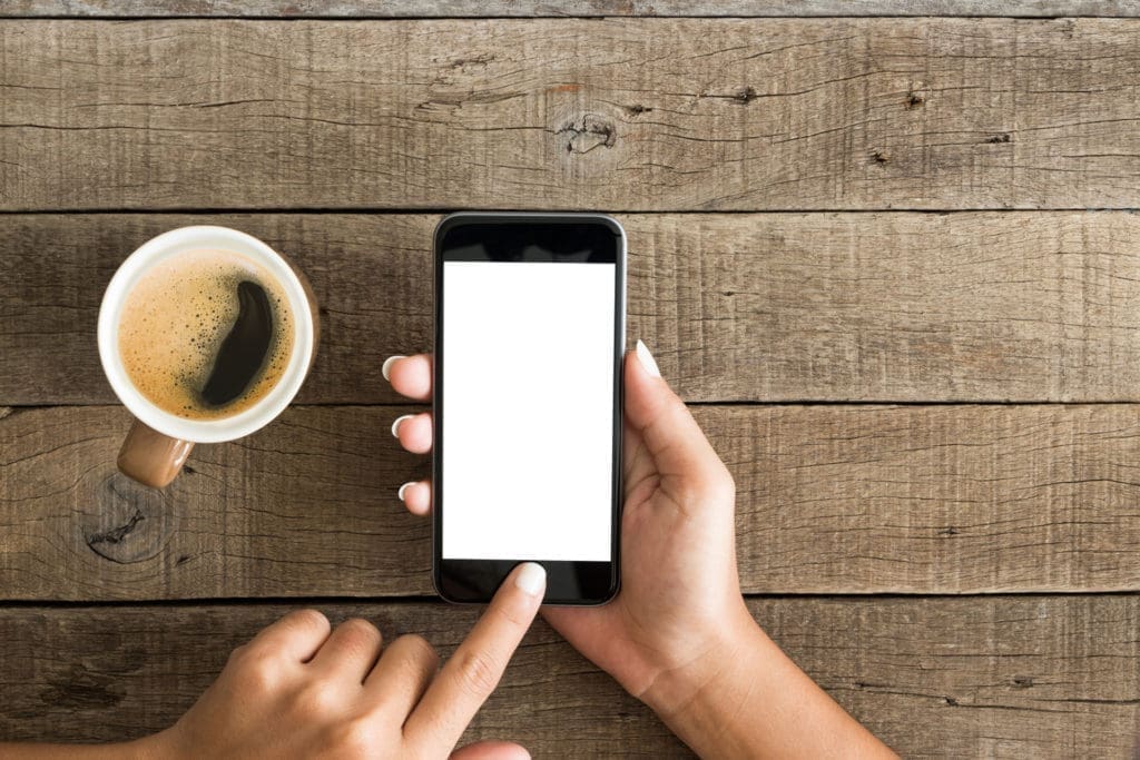 Hand tapping phone beside cup of coffee