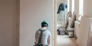 A man in grey shirt and green helmet standing next to wall.