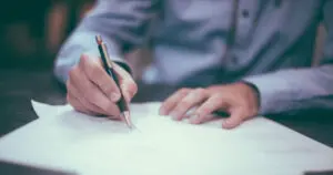 A person writing on paper with a pencil.