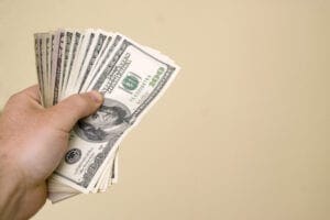 A hand holding a stack of money in front of a wall.