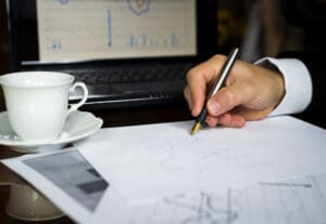 A person writing on paper with a cup of coffee.