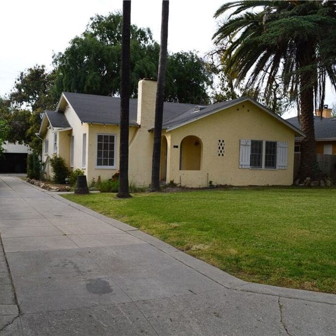 A yellow house with palm trees in the background.