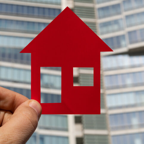 Symbolic red house on a man's hand against the background of a modern high-rise building