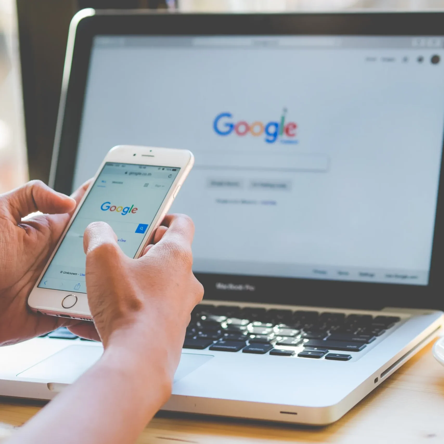 Hands using smartphone with Google on laptop