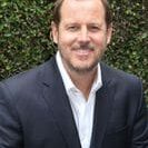 Smiling man wearing navy blazer by hedge