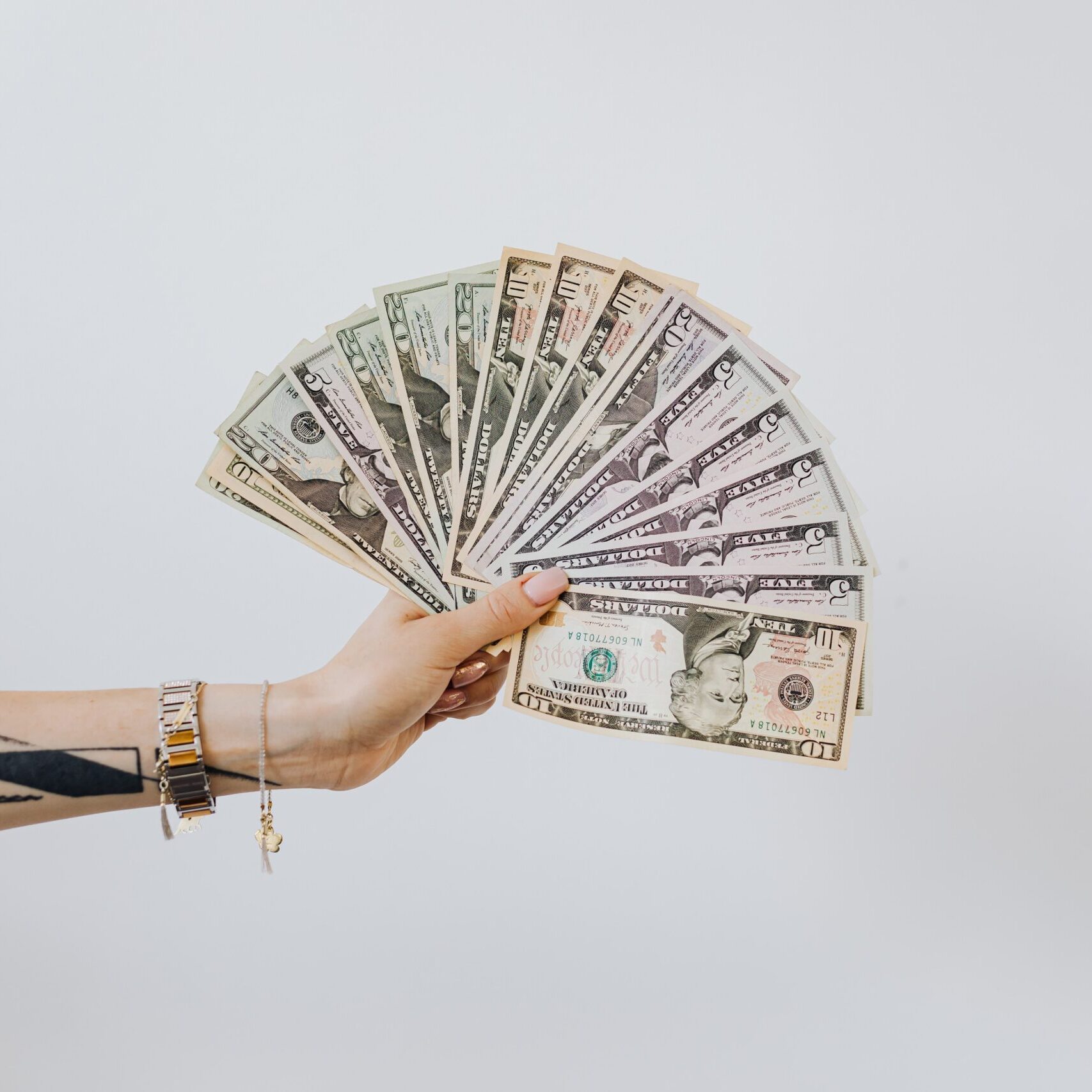 A hand holding money in front of a white wall.
