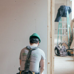A man in grey shirt and green helmet standing next to wall.