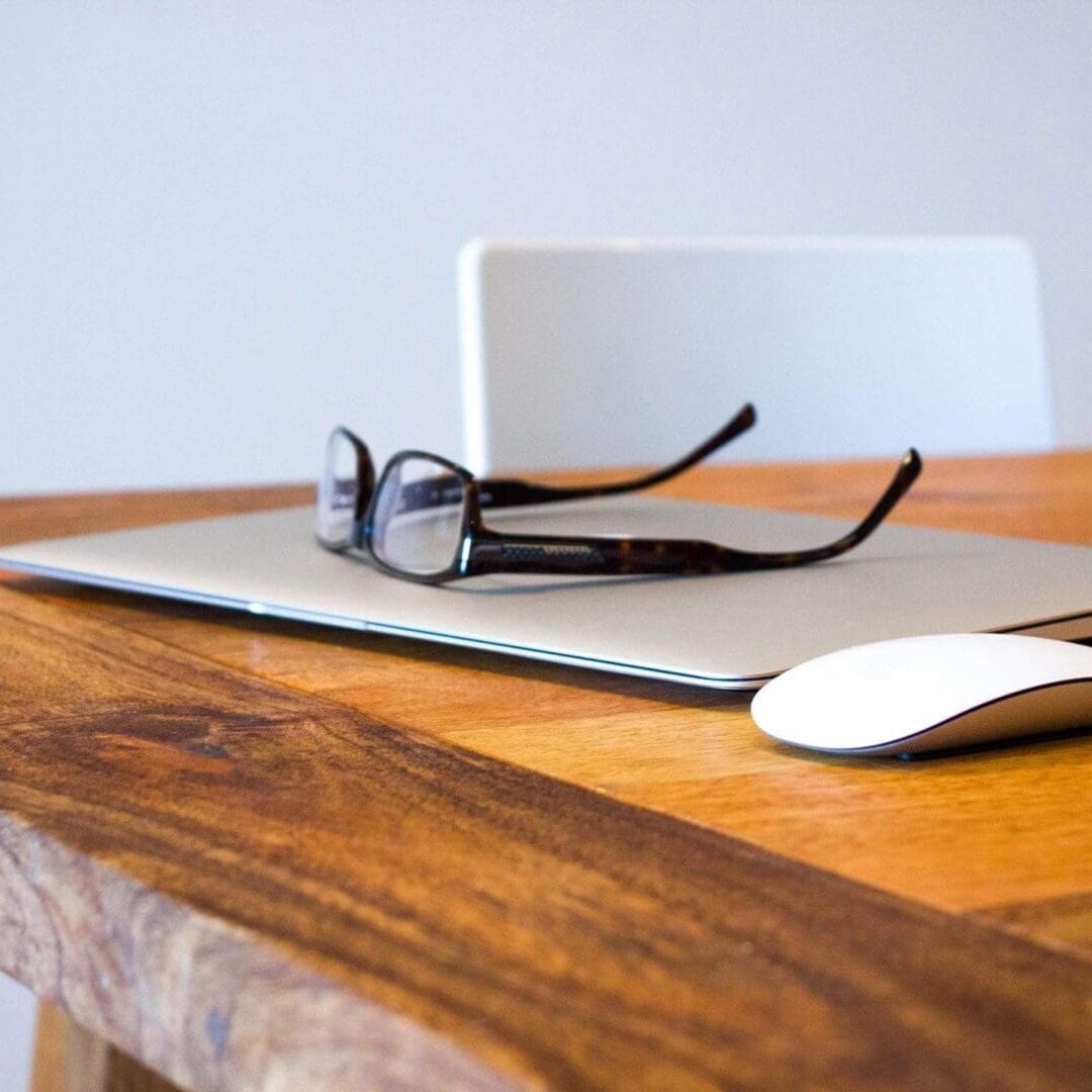 A laptop and glasses on top of a wooden table.